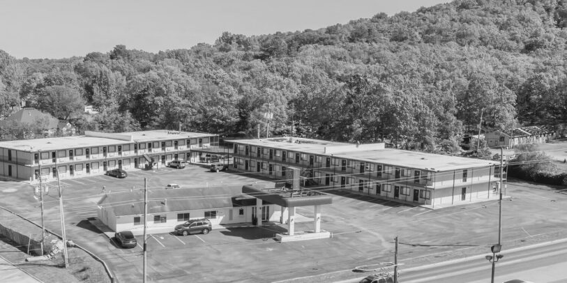Black and white aerial shot of a roadside motel with surrounding forested hills.