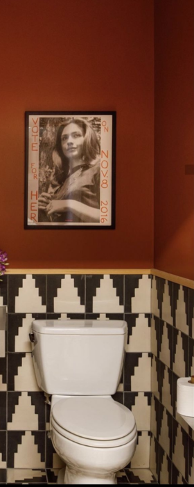 A stylish bathroom with terracotta walls, black and white geometric tiles, a toilet, and a framed political poster.