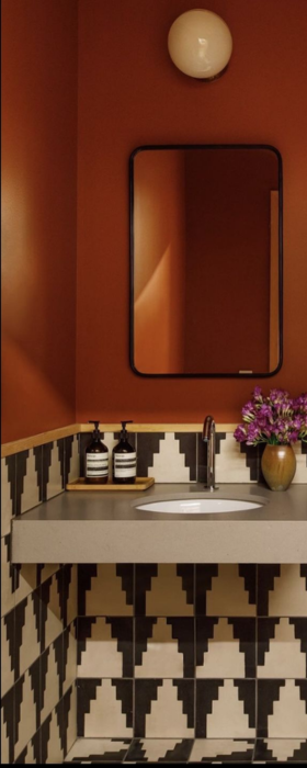 A modern bathroom vanity with a concrete sink, terracotta walls, geometric tiles, and a mirror above.